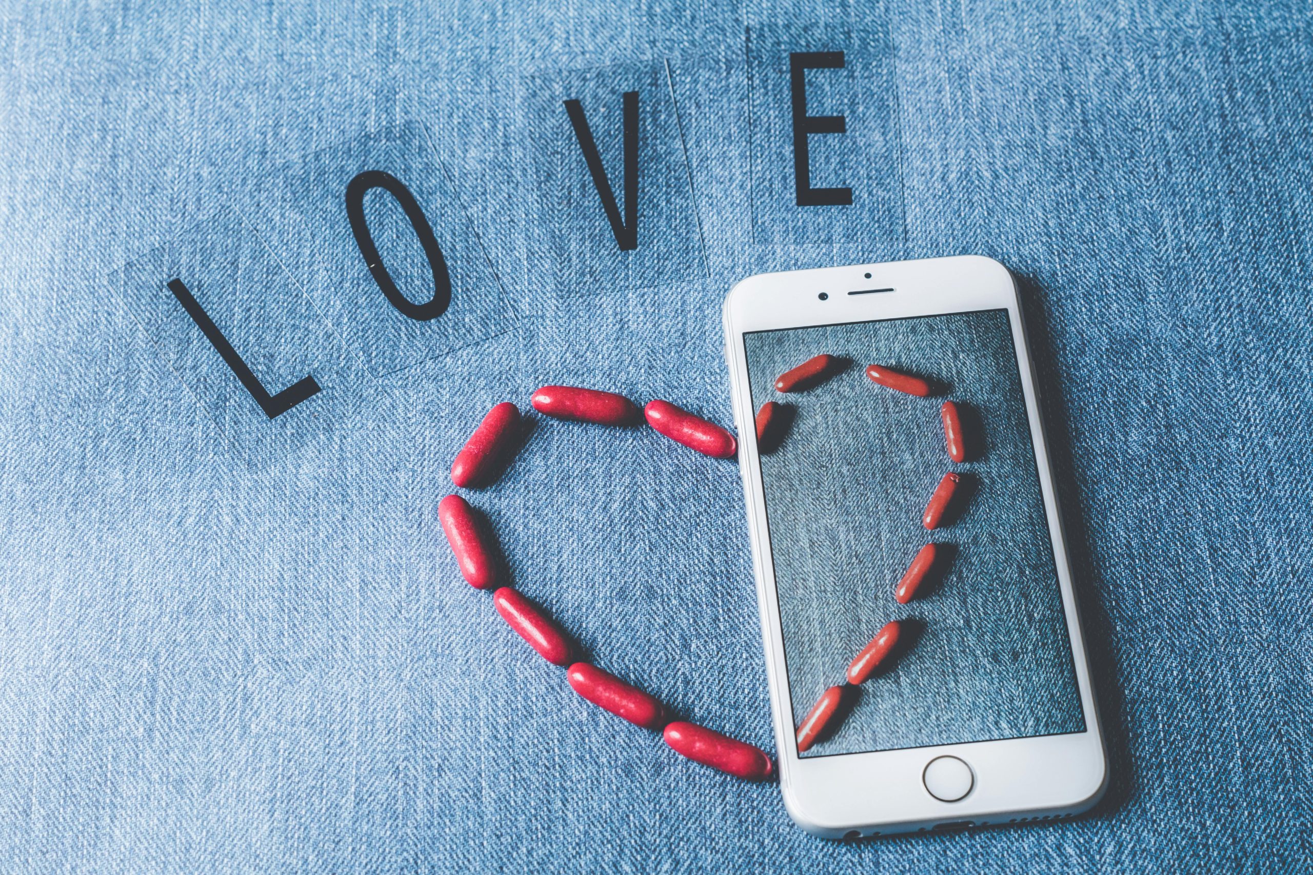 Red pills shaped into a heart on a smartphone, symbolizing love and technology.
