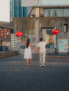 A couple walks hand in hand holding heart-shaped balloons, symbolizing love.