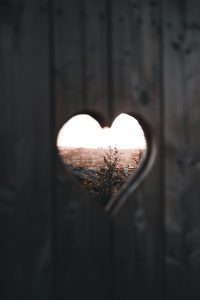 A heart-shaped cutout in a wooden fence reveals a scenic view of a natural landscape at twilight.